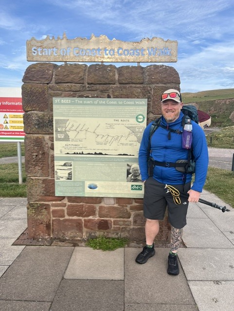 Ady in walking gear soot next to the start sign of the trek