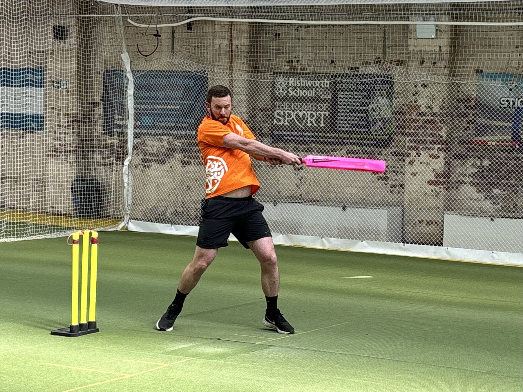 Man batting a cricket ball in orange t shirt